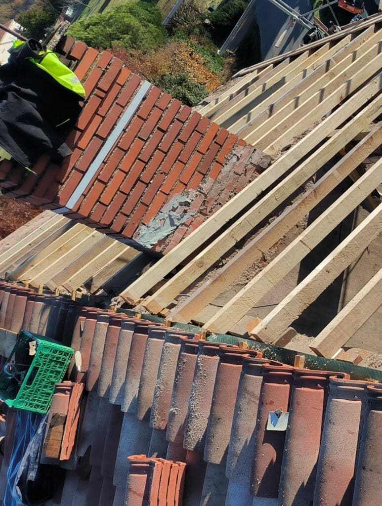 Charpente et toiture en rénovation, installation des tuiles. Charpente de toit en bois brut posée à côté d'un mur en briques rouges. Anciennes tuiles en terre cuite empilées.